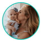 a baby girl wearing a blue bow and dress is held by her mother who kisses her cheek