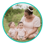 a mother and her twin infant sons sit on the grass all wearing pink outfits