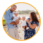 a male female couple stands on a beach holding their twin baby girls