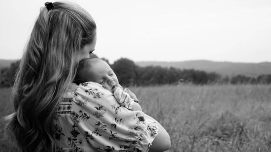 a black and white image of a mother holding her newborn baby against the backdrop of a field of grass