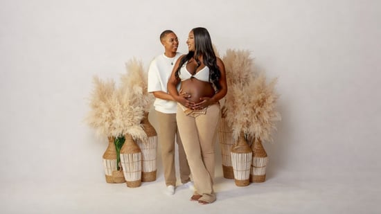 Azavier and Lauren, an LGBTQ+ couple who pursued IVF at Illume Fertility, pose together during a maternity photo shoot, cradling Azavier's pregnant belly.