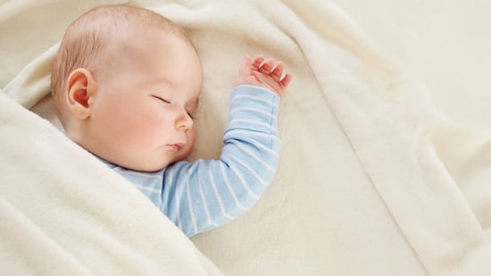 baby boy sleeping in blue and white striped pajamas on beige bedding