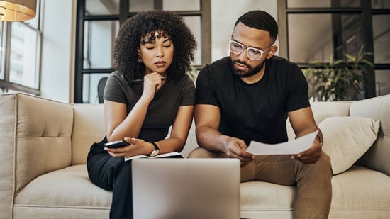 black couple wearing black t-shirts sitting on beige couch researching ivf treatment options