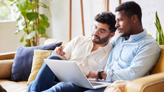 gay male couple sitting on couch next to each other looking at a laptop and taking notes