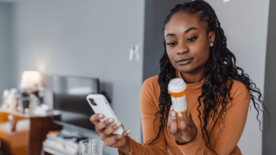 black woman in orange long sleeved top with braids looking at medication bottle