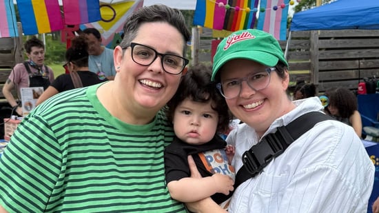 a lesbian couple smiling holding their infant son at an outdoor event