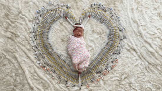 newborn baby girl wrapped in rainbow patterned blanket laying on white fluffy blanket surrounded by IVF shots in shape of heart