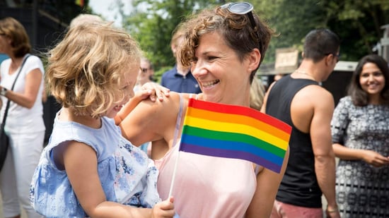 lgbtq mom holding young daughter at pride parade smiling