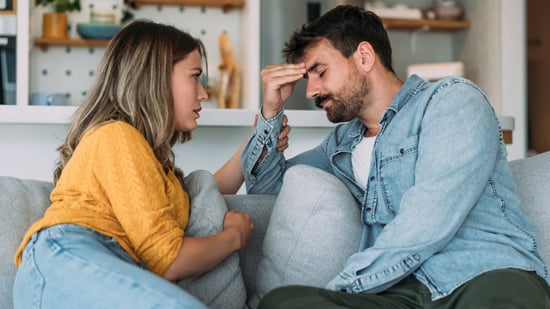 man and woman sitting on couch talking and looking worried