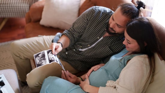 male female couple sitting on couch holding ultrasound picture 