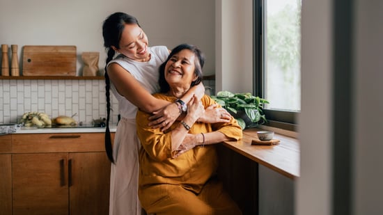 asian mother and daughter smiling and hugging next to bright window
