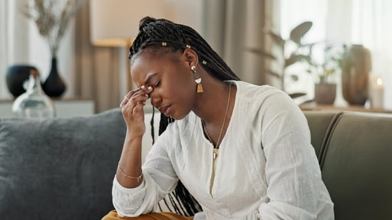 a Black woman sits at home feeling stressed and anxious about infertility issues