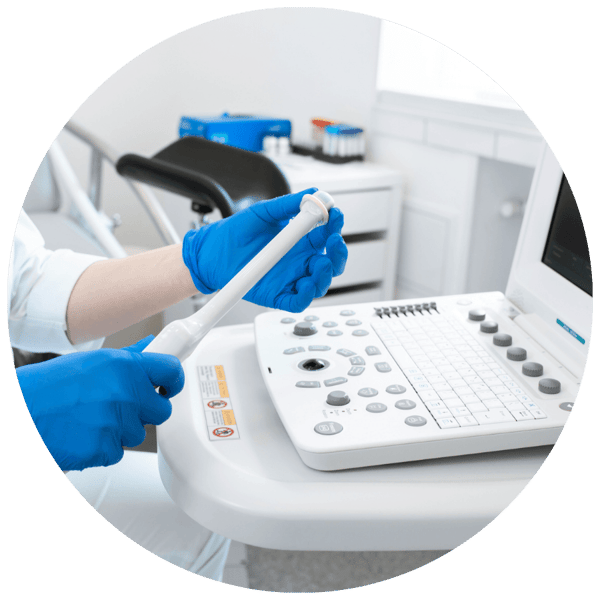 Clinician holding a transvaginal ultrasound probe beside an ultrasound machine in an exam room.
