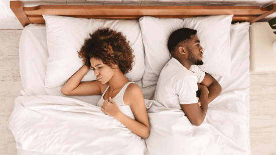 unhappy couple laying back to back in bed with white sheets