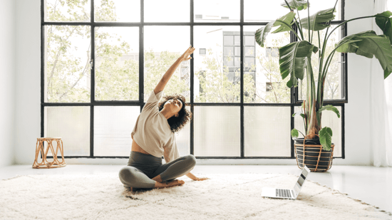 yoga for fertility woman stretching right arm over head in seated position in front of large paned window